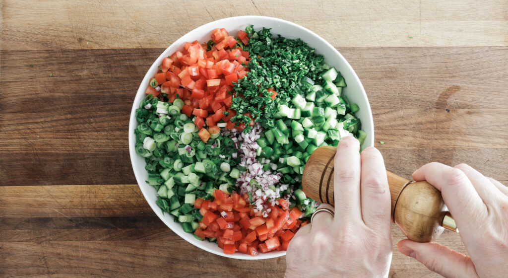 seasoning the ingredients of a middle eastern salad in a bowl