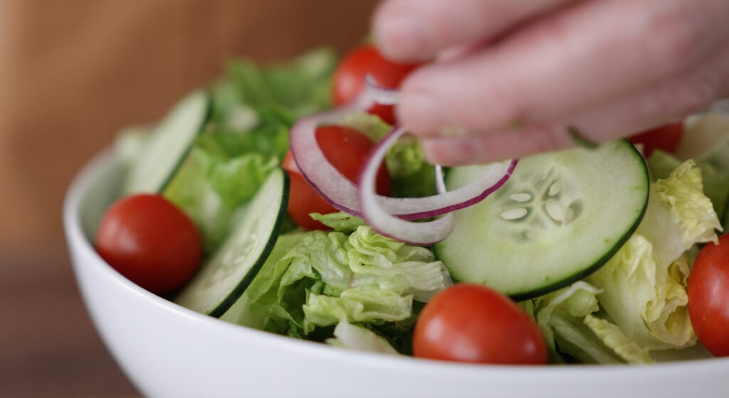 Close up of red onions being placed on the salad