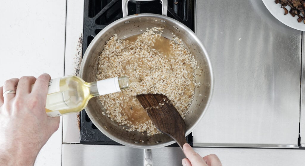 Pourings white win into the pan while stirring with a wooden utensil