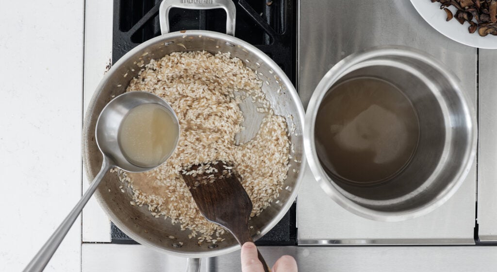 adding a ladle full of stock to the pot with risotto