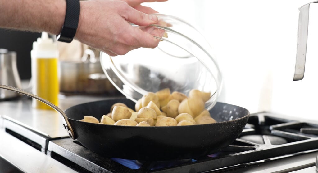 pouring potatoes into a black pan