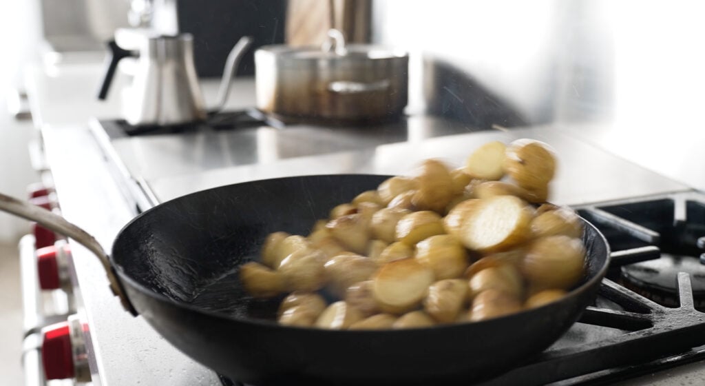 Tossing potatoes in a black pan
