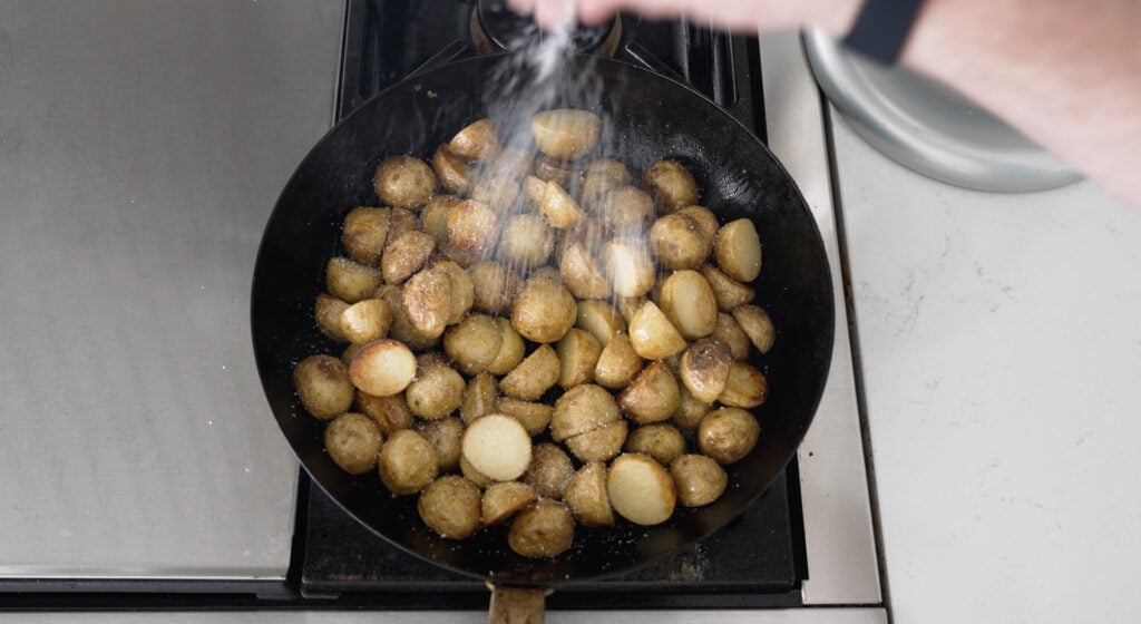 Sprinkling salt. on lightly browned potatoes