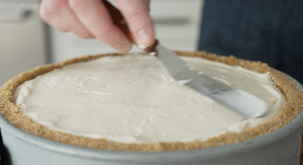 using an offset spatula to smooth the top of the cheesecake