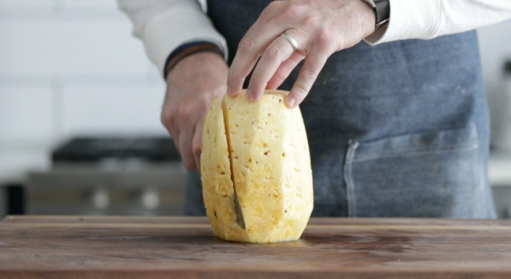 slicing a peeled pineapple on a cutting board
