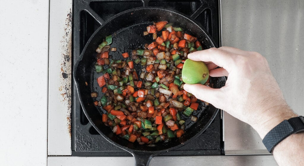 a hand squeesing a lime into a cast iron pan with veggies in it