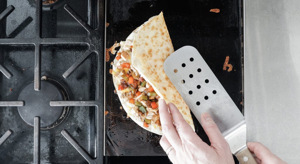 using a turner to fold the quesadilla in half so all of the ingredients are on the inside