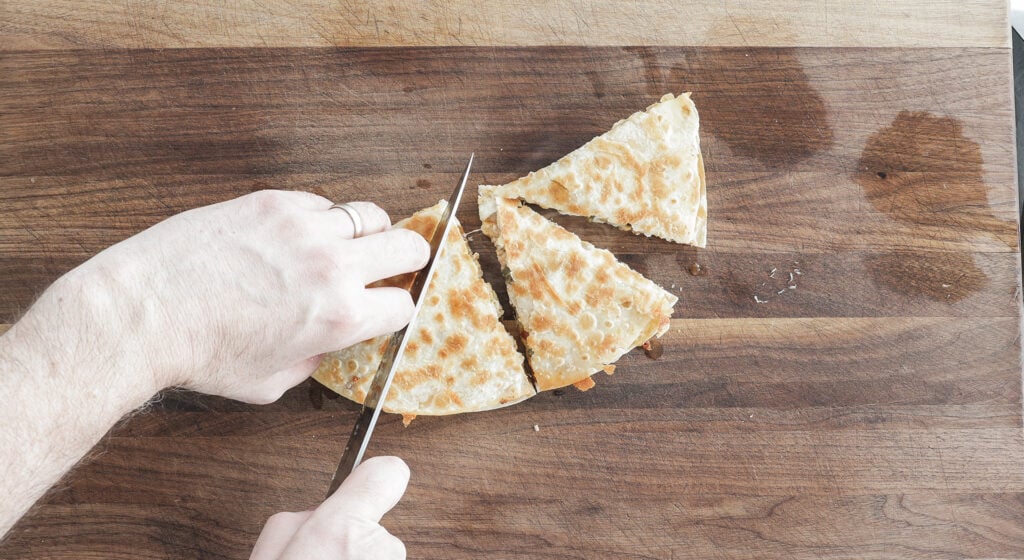 a knife being use to cut the quesadilla into 4 triangles 