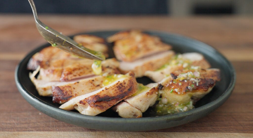 marinade dripping off of a spoon onto a plate with sliced chicken on it