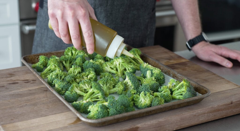 Using a squeeze bottle to drizzle oil on the broccoli