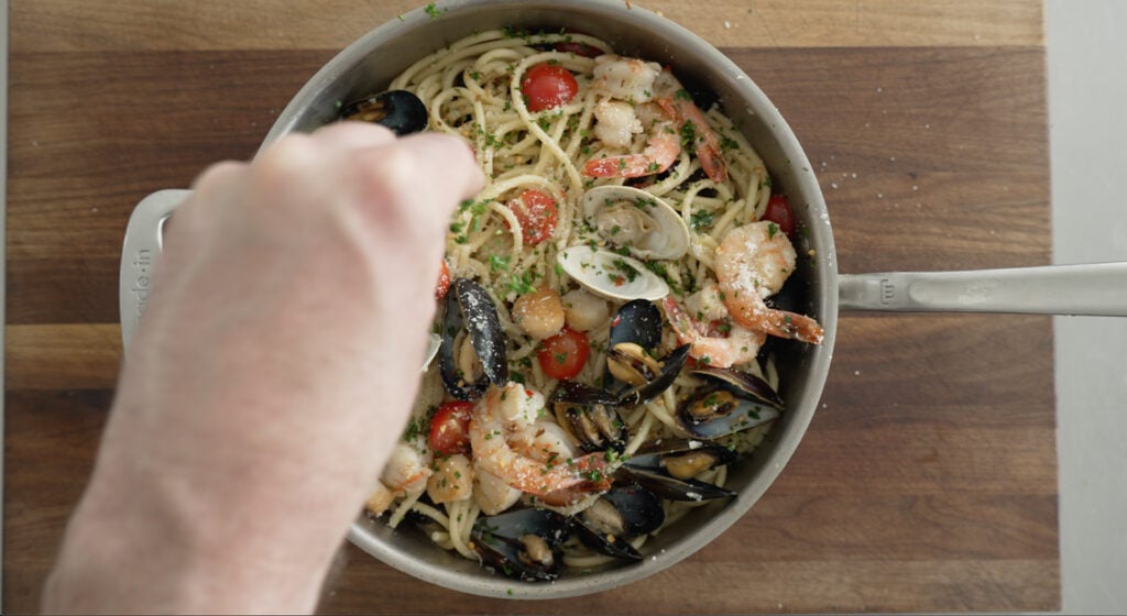 Sprinkling fresh parsley on top of the seafood pasta in a pan