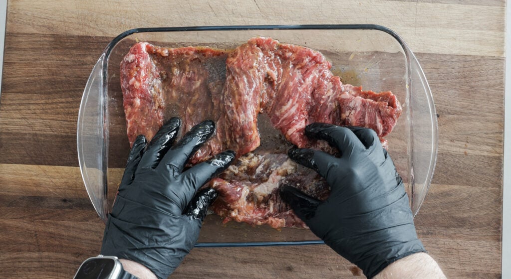 Gloved hands massaging marinade into the steak