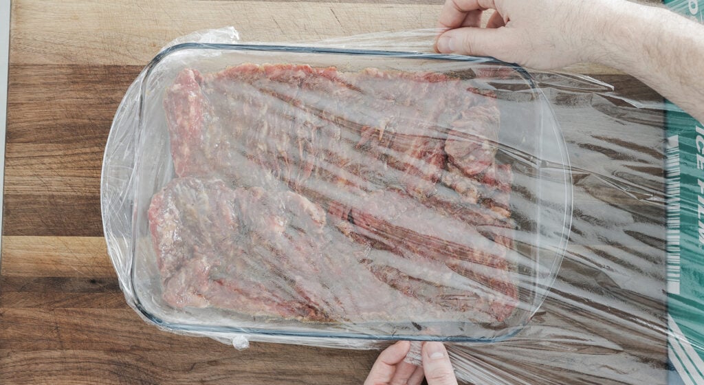 covered skirt steak in marinade in a casserole dish