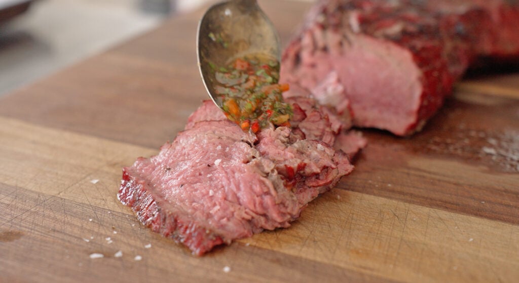 Spooning chimichurri sauce on top of the cooked tri tip