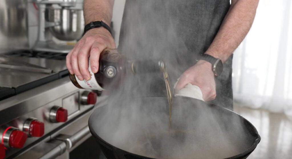 Pouring cognac into a steaming hot pan held away from the stove