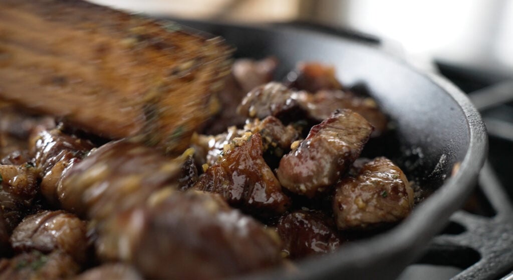 Steak bites in a pan with small pieces of garlic visible
