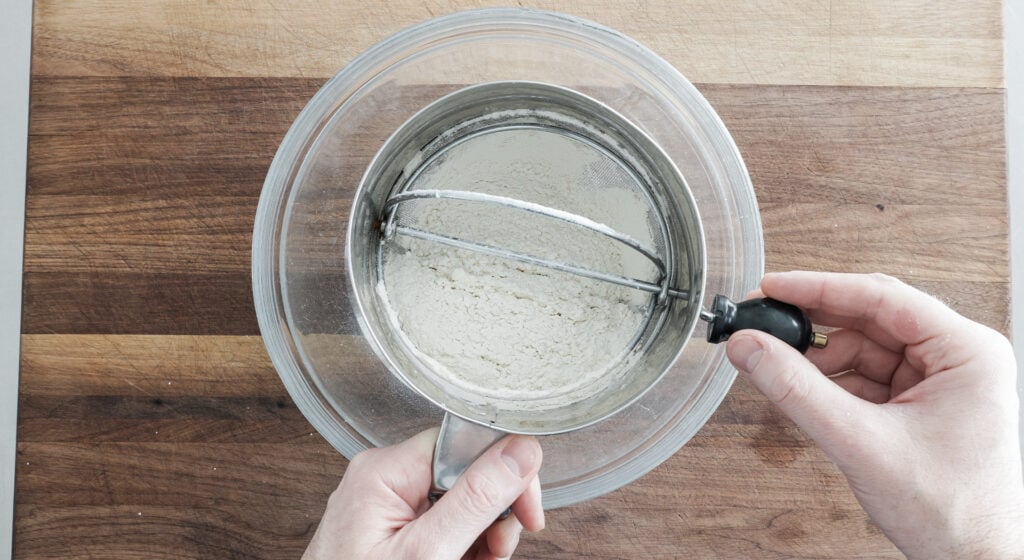using a sifter to sift dry ingredients into a bowl