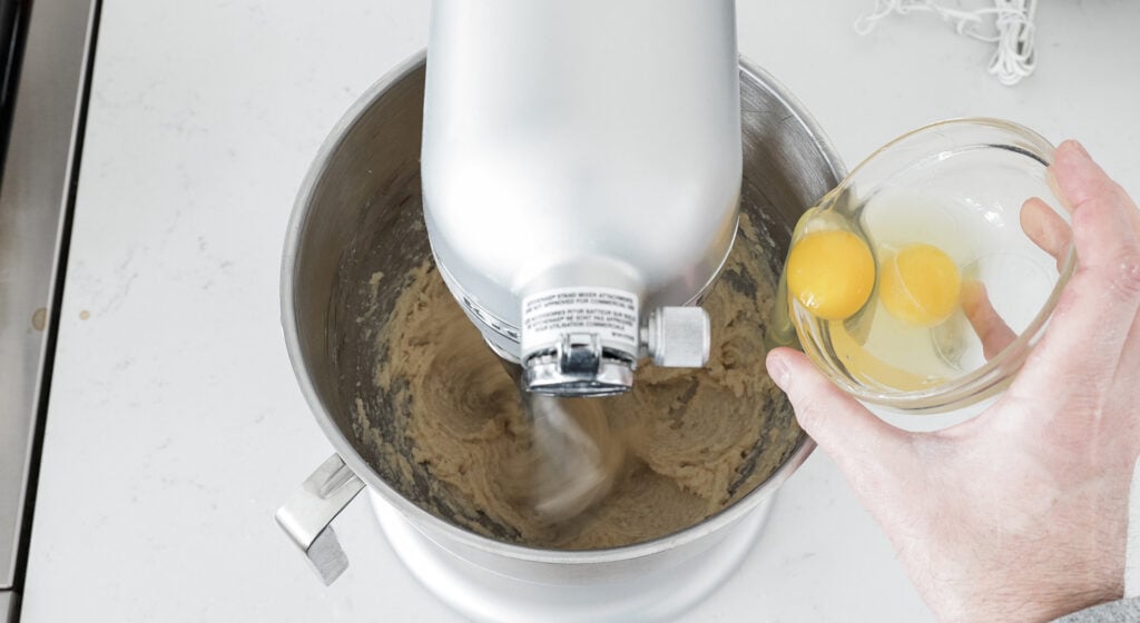 Dropping one egg from a glass bowl into the bowl of the stand mixer