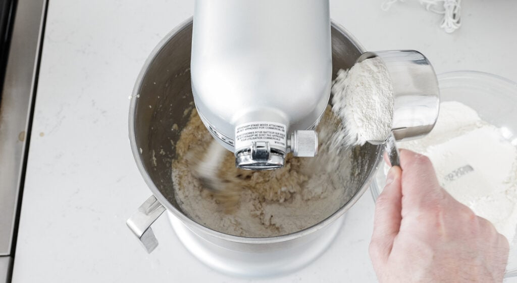 Adding a measuring cup full of the dry ingredients to the bowl of the stand mixer