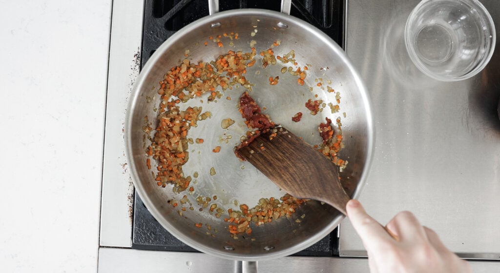 tomato paste added to the pot being stirred with a wooden utensil