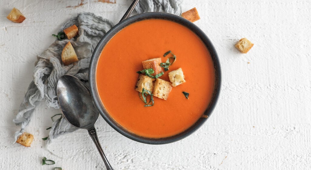 Finished bowl of tomato soup with croutons and basil on top