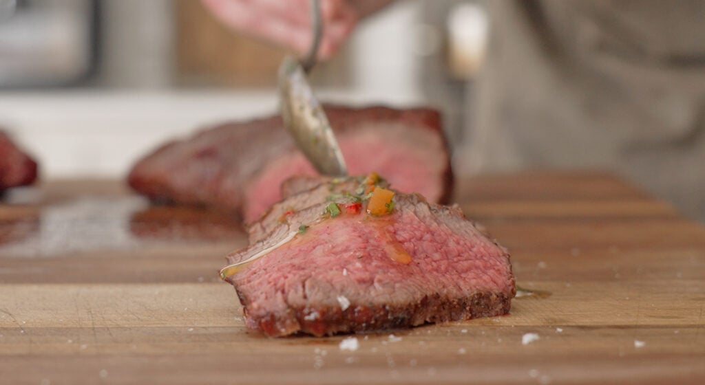 a piece of steak being topped with chimichurri sauce
