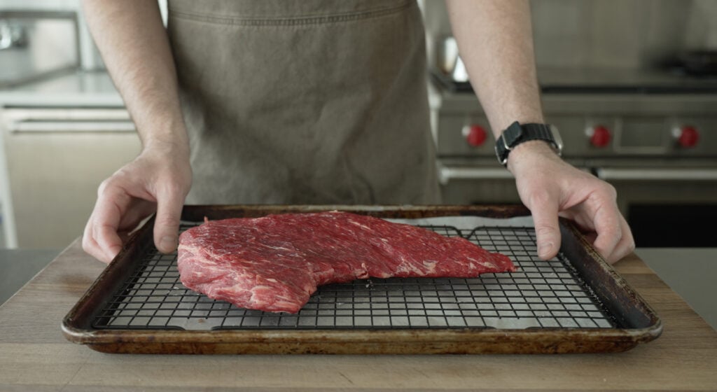 a steak on a wire rack over a sheet tray being placed on a table