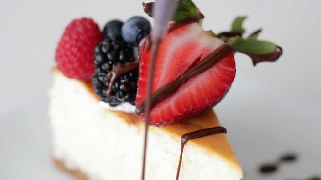 a slice of cheesecake with berries and choco sauce on top