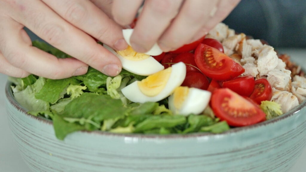 adding tomatoes and eggs to a salad