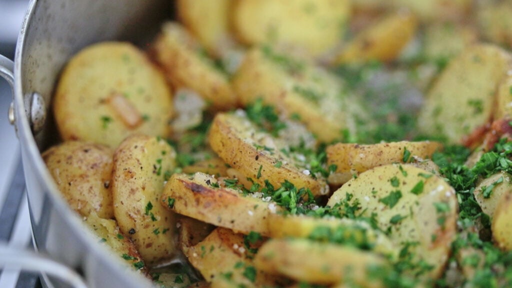 adding parsley to a pan of cooked potatoes