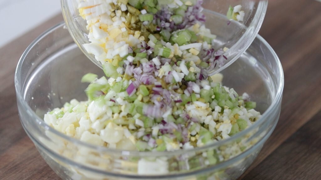 adding chopped ingredients to a bowl of potato salad
