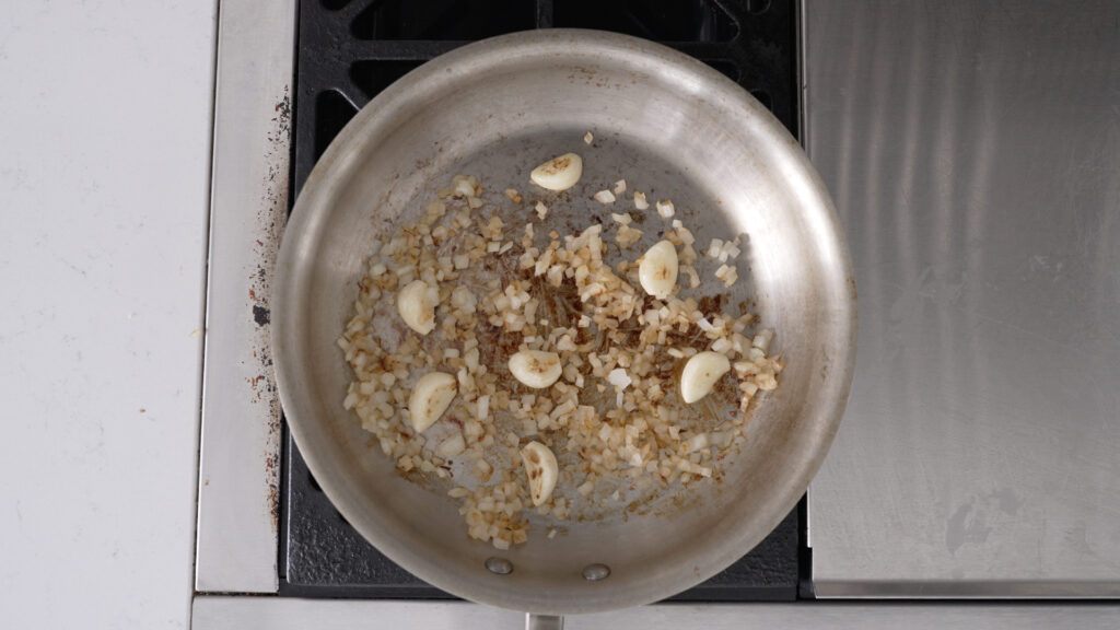 overhead view of  browned onions and garlic cloves in a pan