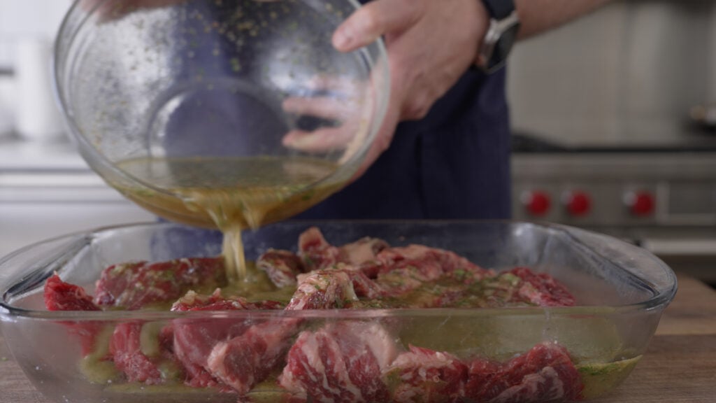 pouring marinade over the steak in a glass container