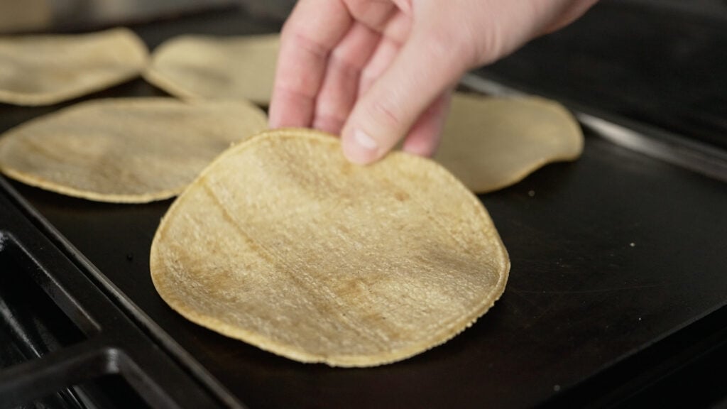 placing a corn tortilla on a griddle
