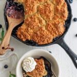 Blueberry cobbler in a skillet with a scoop in a bowl