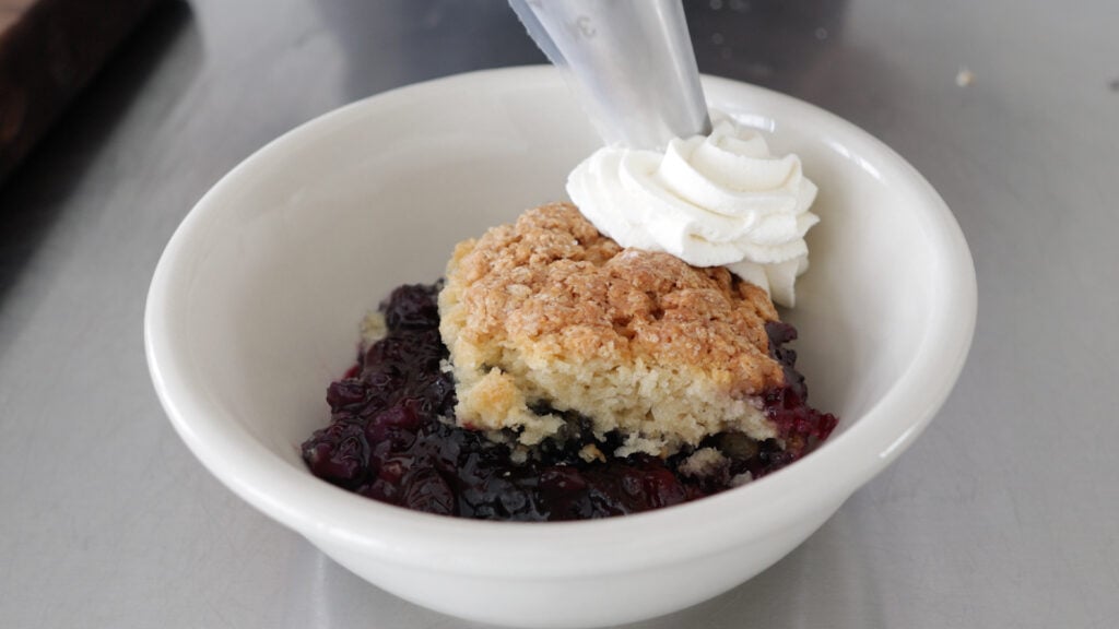 Adding whipped cream to a serving of blueberry cobbler