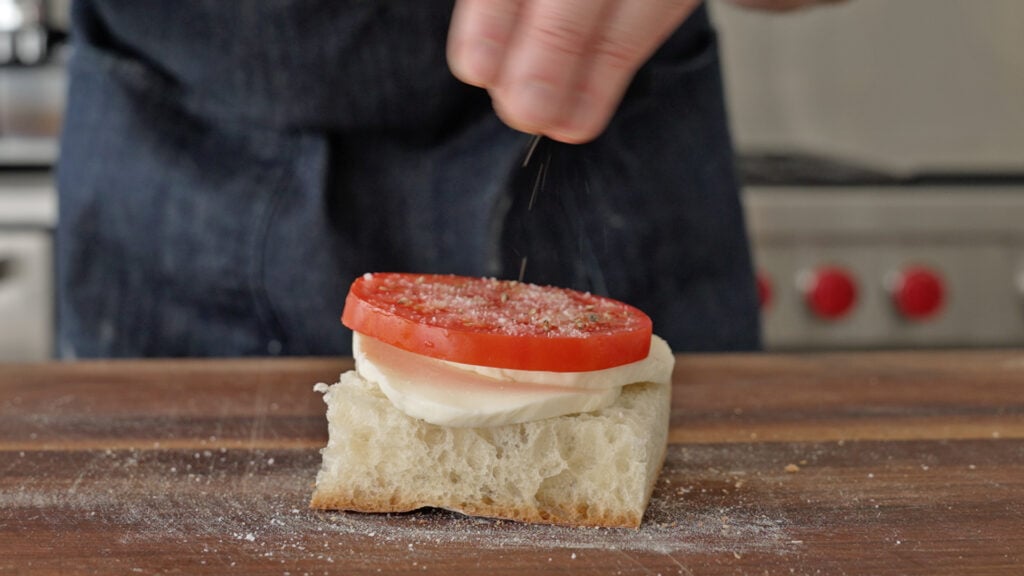 Sprinkling salt on top of a tomato on the sandwich