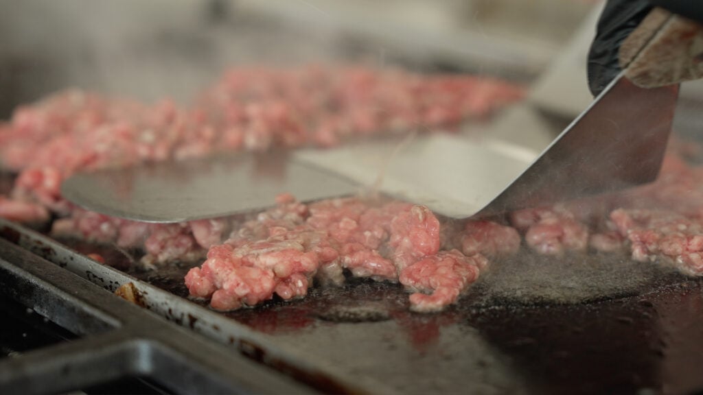Using two spatulas to flatten the beef on a griddle