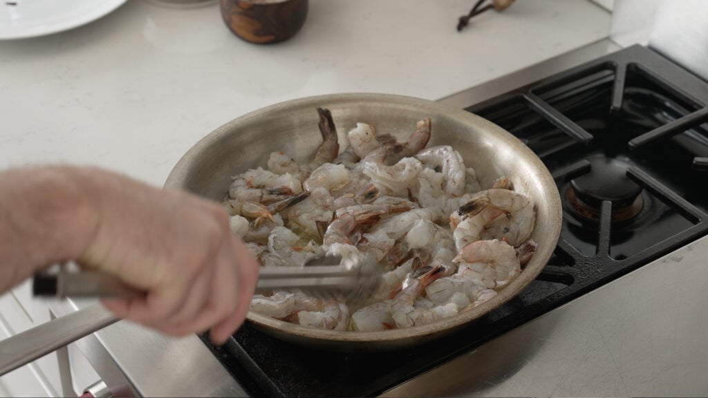 using tongs to add shrimp to the pan