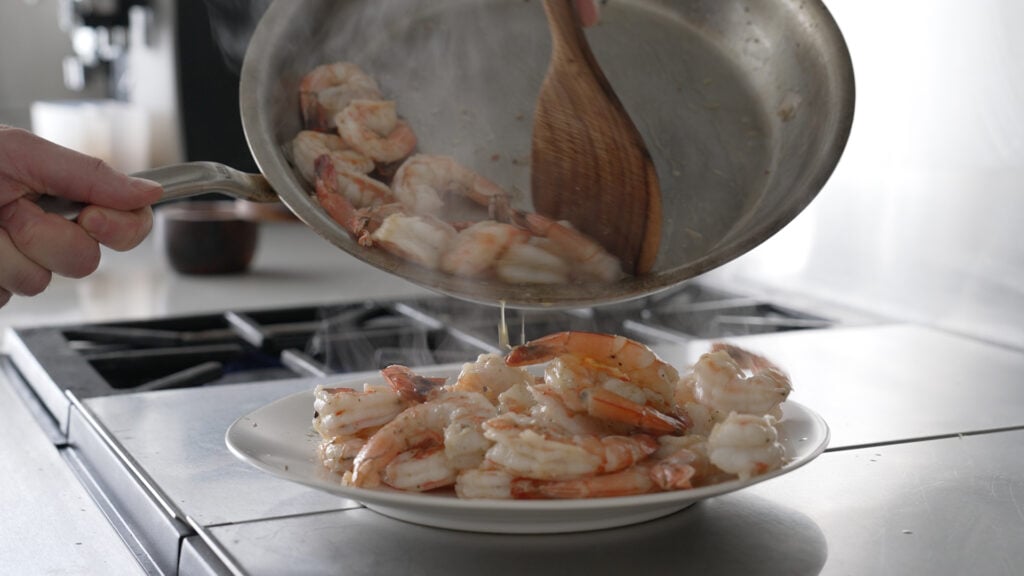 pouring the shrimp from the pan onto a plate