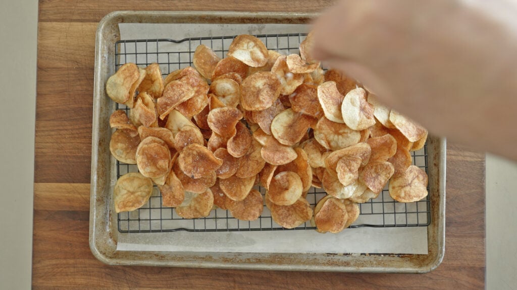 sprinkling the cooked potato chips with salt