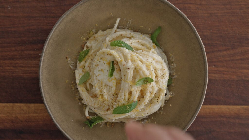 Finished pasta in a serving bowl topped with fresh basil leaves