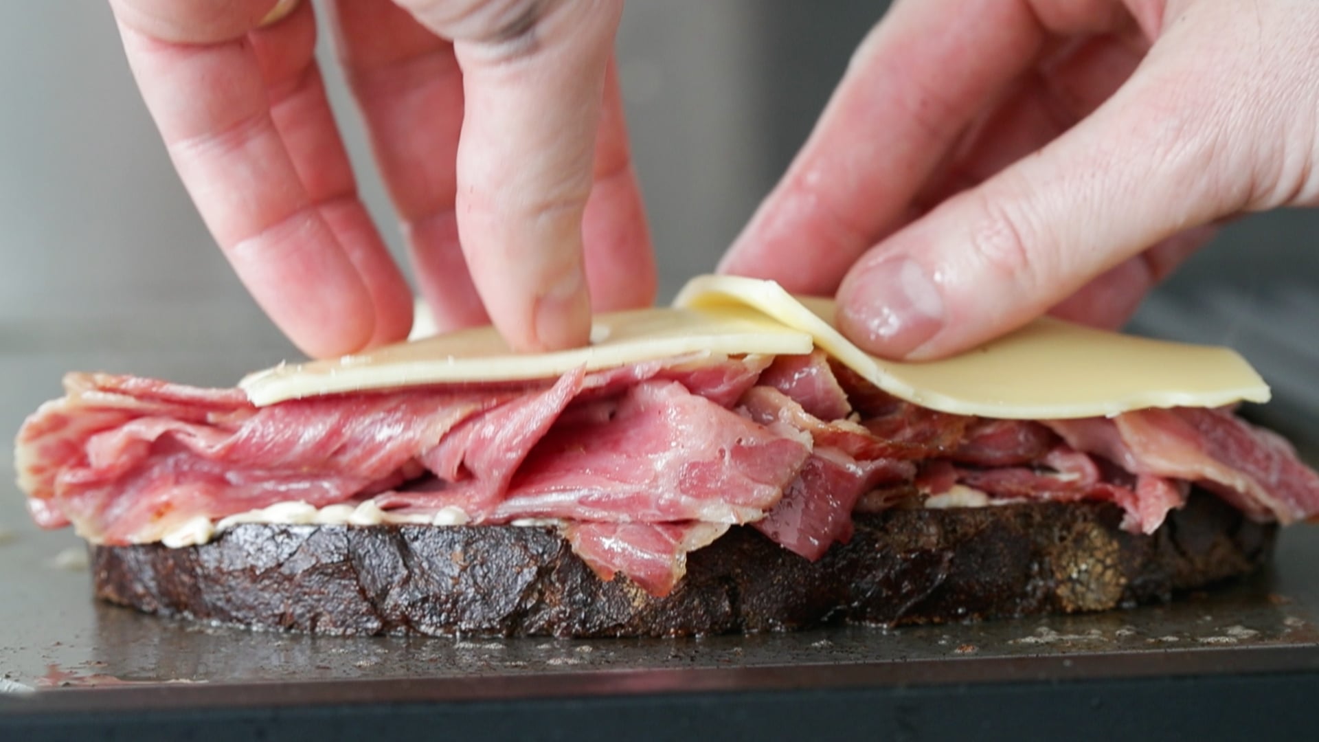 adding cheese and sauerkraut to a reuben sandwich