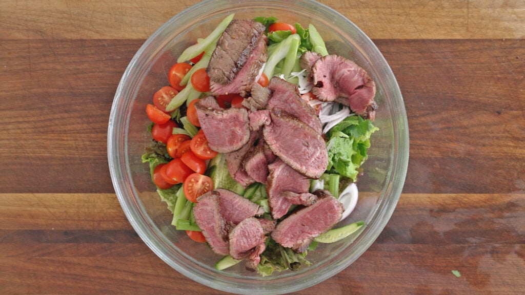 slices of steak on top of the salad