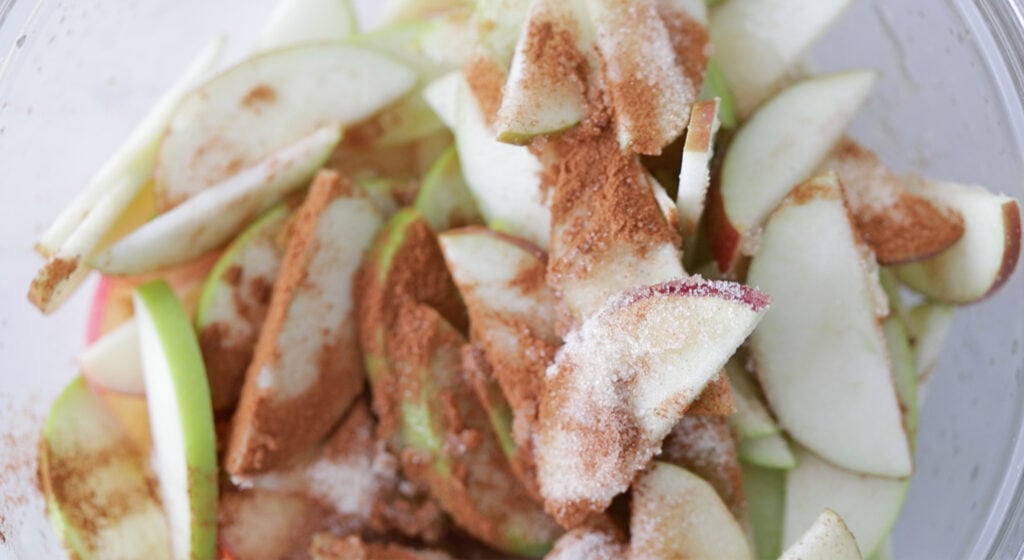 mixing sliced apples with cinnamon and sugar in a bowl