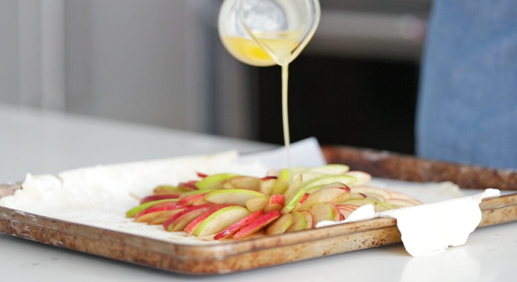 adding melted butter to the top of an apple galette
