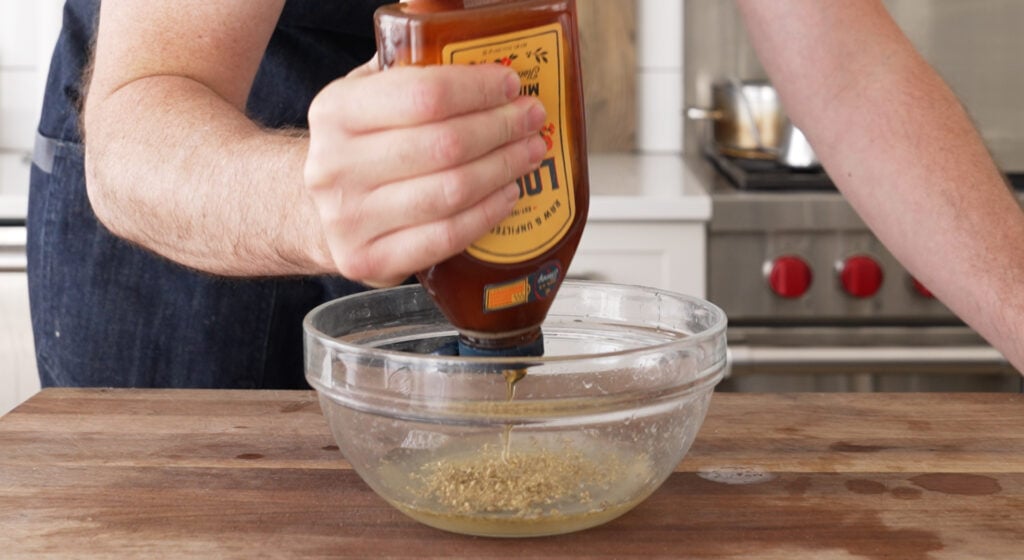 adding honey to a bowl with vinegar and oregano