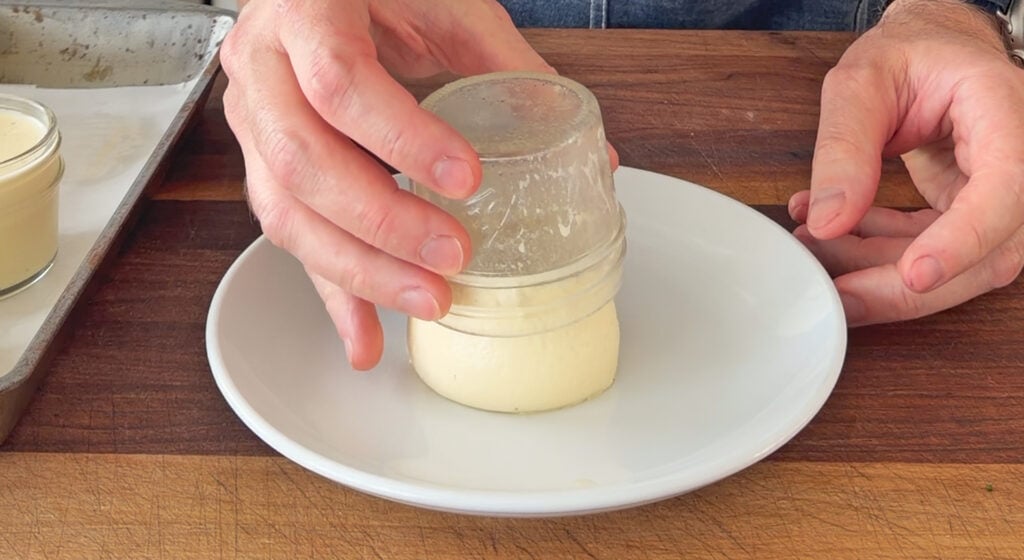 Inverting a jar of homemade panna cotta onto a white serving plate.