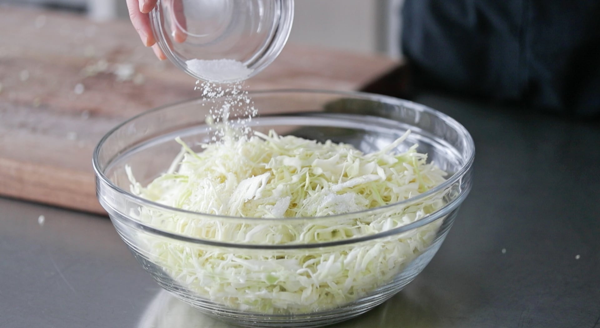 adding salt to a bowl of cabbage