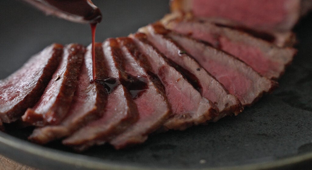 pouring red wine sauce on top of steak slices